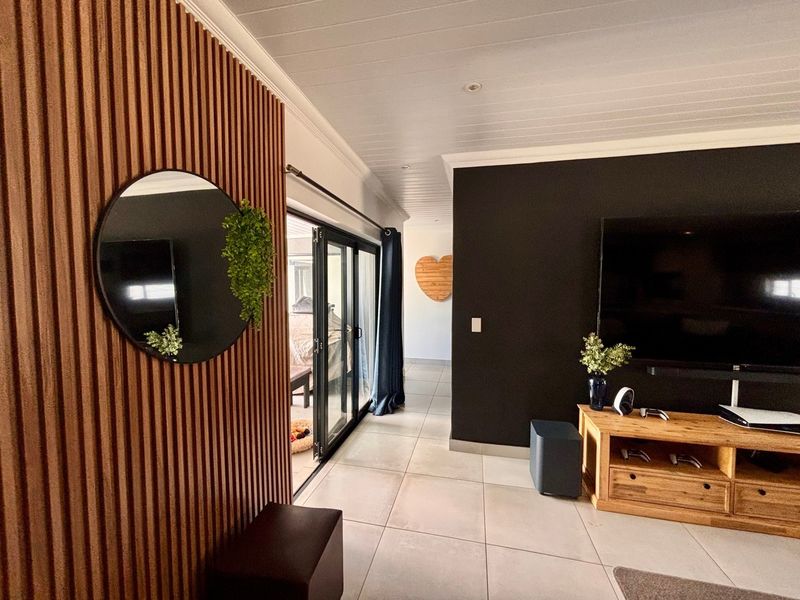 Modern living room featuring stylish slatted timber wall paneling, large format floor tiles, and black aluminium sliding doors leading to an outdoor area.