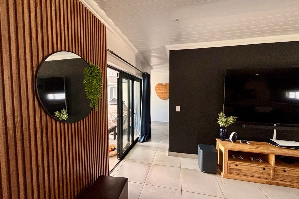 Modern living room featuring stylish slatted timber wall paneling, large format floor tiles, and black aluminium sliding doors leading to an outdoor area.