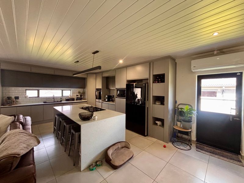 Modern open-plan kitchen featuring a central island with gas hob, sleek cabinetry, subway tile backsplash, and tiled flooring under a stylish tongue and groove ceiling.