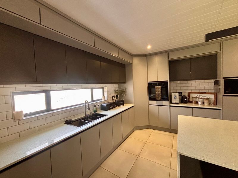Modern kitchen featuring sleek grey cabinetry, stone countertops, subway tile backsplash, and integrated oven, complemented by neutral ceramic floor tiles.