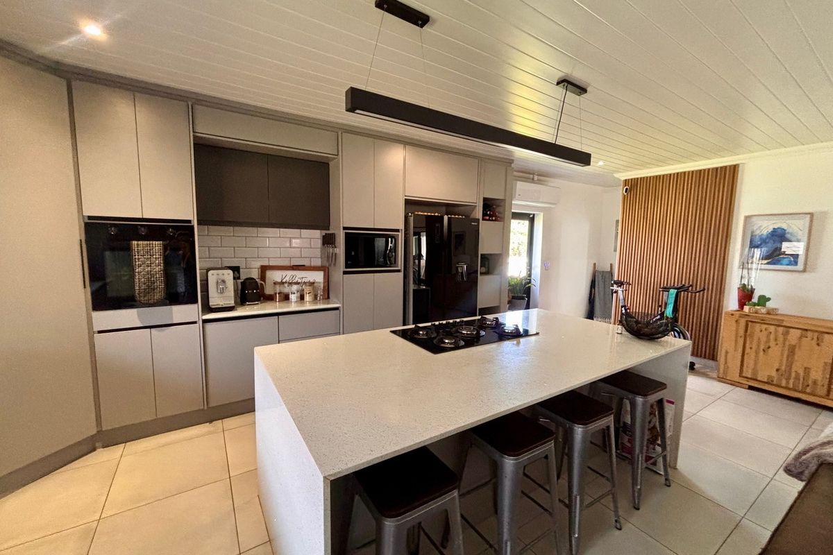 Modern kitchen featuring a large central island with a gas cooktop, sleek cabinetry, subway tile backsplash, and a stylish timber slat feature wall.