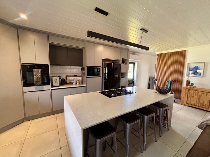 Modern kitchen featuring a large central island with a gas cooktop, sleek cabinetry, subway tile backsplash, and a stylish timber slat feature wall.