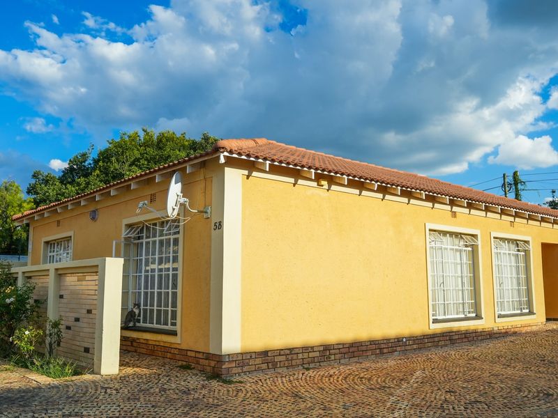 A well-maintained single-story house featuring a yellow stucco facade, tiled roof, security bars on windows, and a paved driveway.