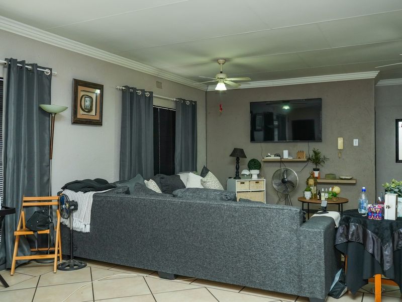 A spacious living room featuring tiled flooring, ceiling fans, and a neutral wall finish, providing a comfortable and functional area for relaxation.