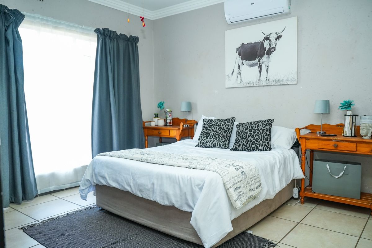 A functional bedroom featuring tiled flooring, a wall-mounted split-system air conditioner, and neutral wall finishes.