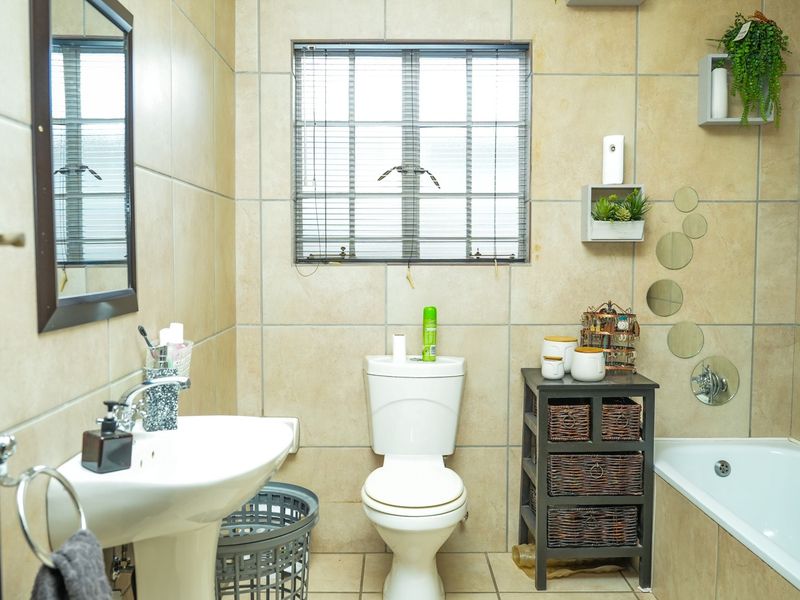 A functional bathroom featuring a pedestal basin, toilet, and bathtub with neutral wall and floor tiling.