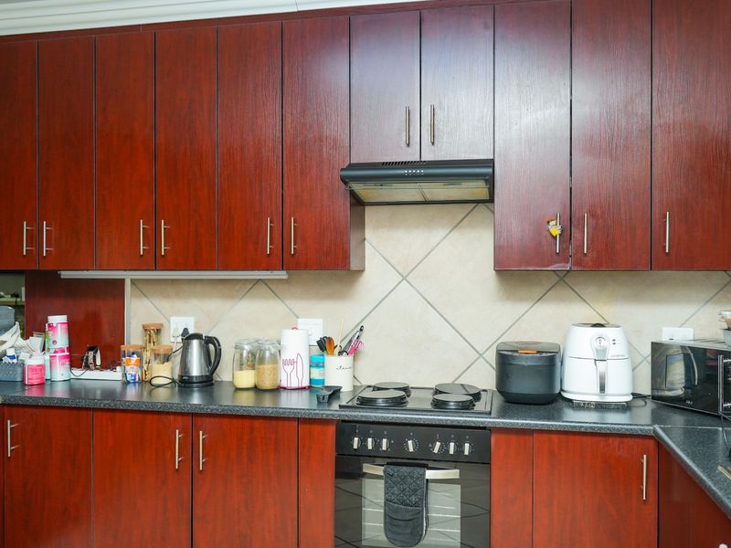 A functional kitchen featuring dark wood-finish cabinetry, laminate countertops, a built-in oven, electric hob, and a tiled backsplash.