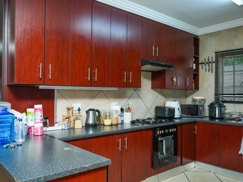 A functional kitchen featuring dark wood-finish cabinetry, laminate countertops, a gas hob, and a built-in oven with a tiled backsplash.
