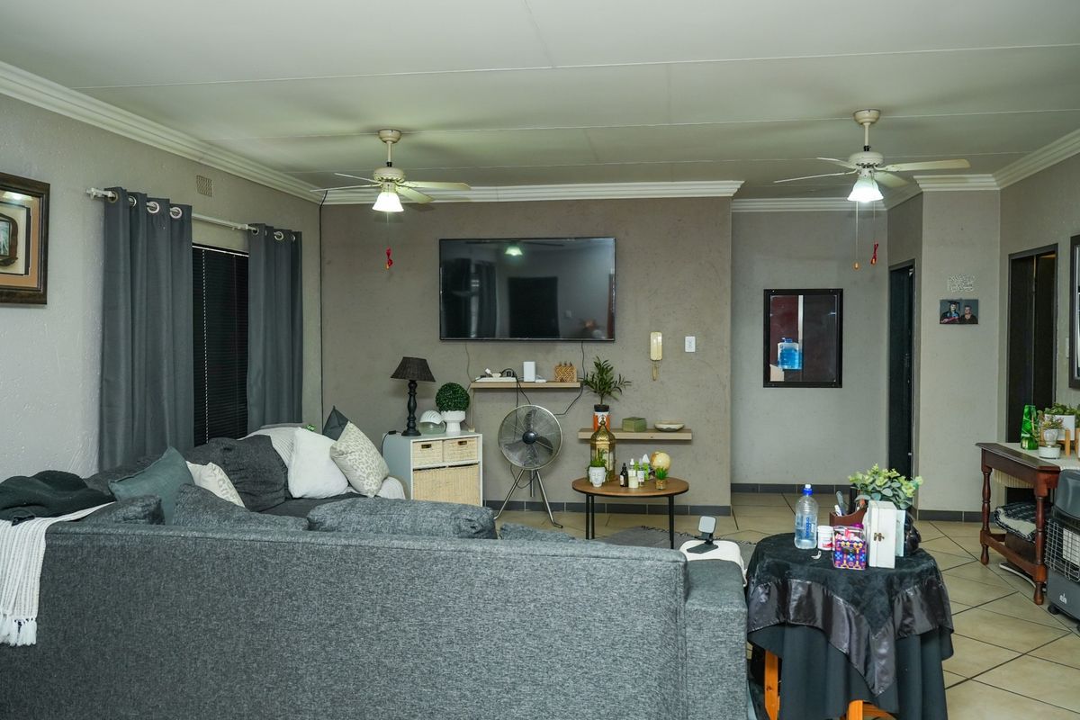 A spacious living room featuring tiled flooring, dual ceiling fans, and coved cornicing, providing a comfortable and functional family living area.