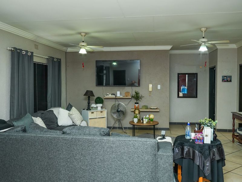 A spacious living room featuring tiled flooring, dual ceiling fans, and coved cornicing, providing a comfortable and functional family living area.