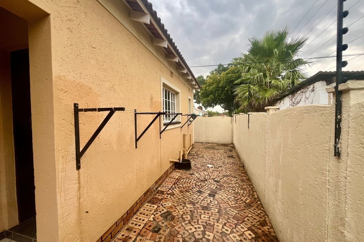 A side exterior walkway featuring brick paving, wall-mounted washing line brackets, and a perimeter wall with electric fencing.
