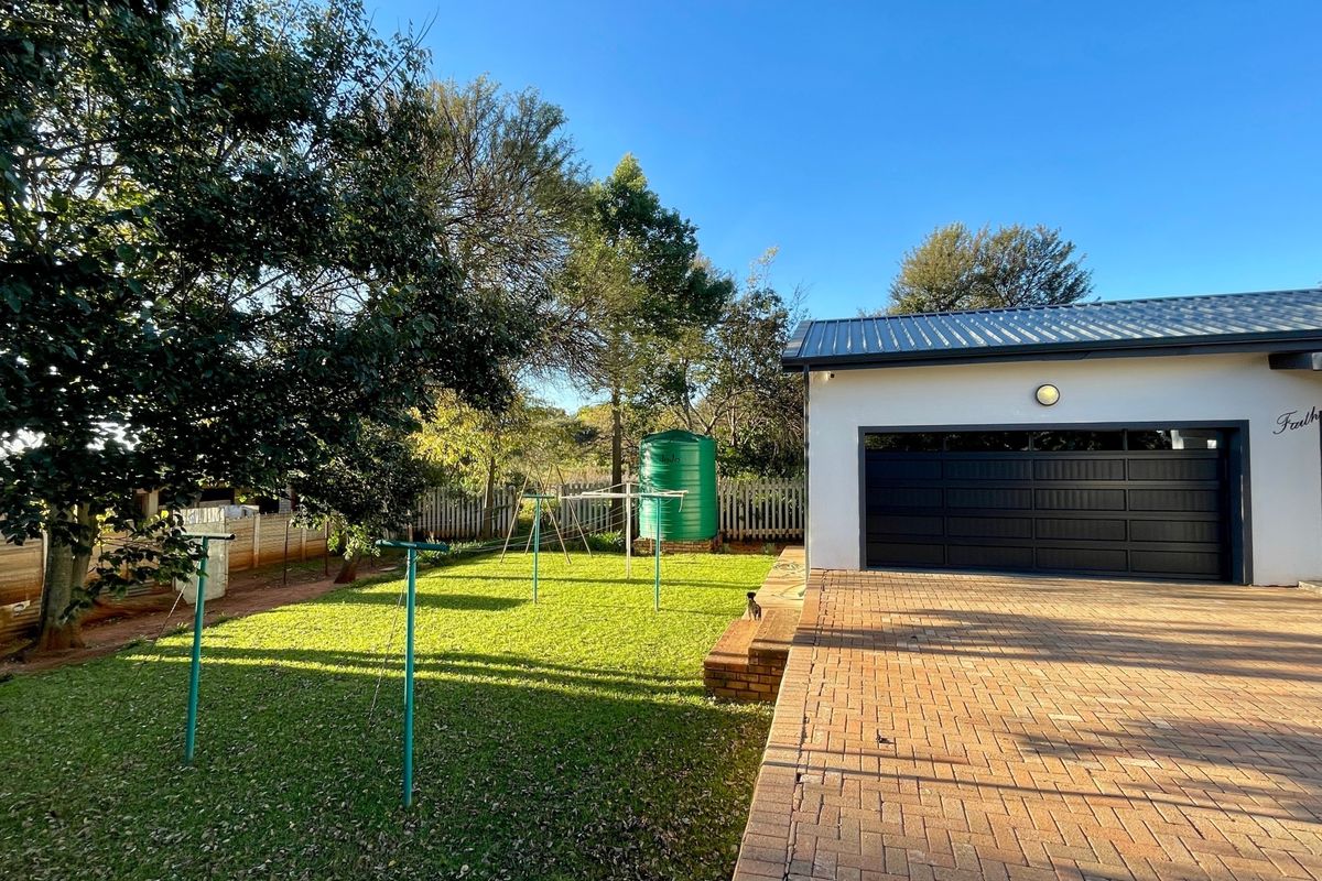 Rear exterior view featuring a brick paved driveway, a modern sectional garage door, and a private garden area with a water storage tank.