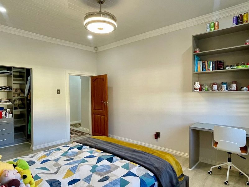 A well-maintained bedroom featuring built-in cabinetry, a desk with shelving, laminate flooring, and a ceiling fan.