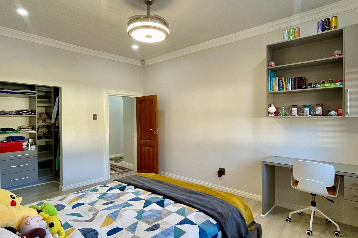 A well-maintained bedroom featuring built-in cabinetry, a desk with shelving, laminate flooring, and a ceiling fan.