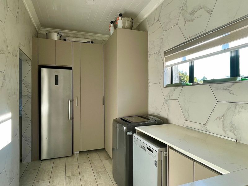 A modern, well-appointed laundry room featuring sleek built-in cabinetry, stone countertops, and stylish hexagon wall tiles.