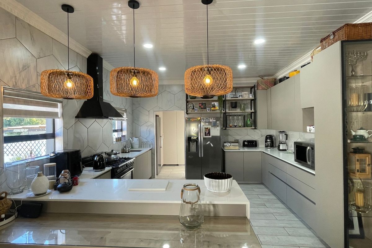 Modern kitchen featuring sleek grey cabinetry, quartz countertops, a gas hob with extractor fan, and stylish pendant lighting, offering a functional and contemporary workspace.