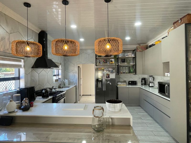 Modern kitchen featuring sleek grey cabinetry, quartz countertops, a gas hob with extractor fan, and stylish pendant lighting, offering a functional and contemporary workspace.