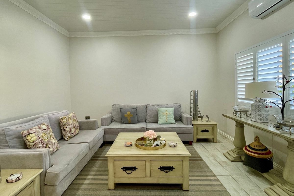 A well-maintained living room featuring tiled flooring, plantation shutters, crown molding, and a tongue and groove ceiling with recessed lighting.