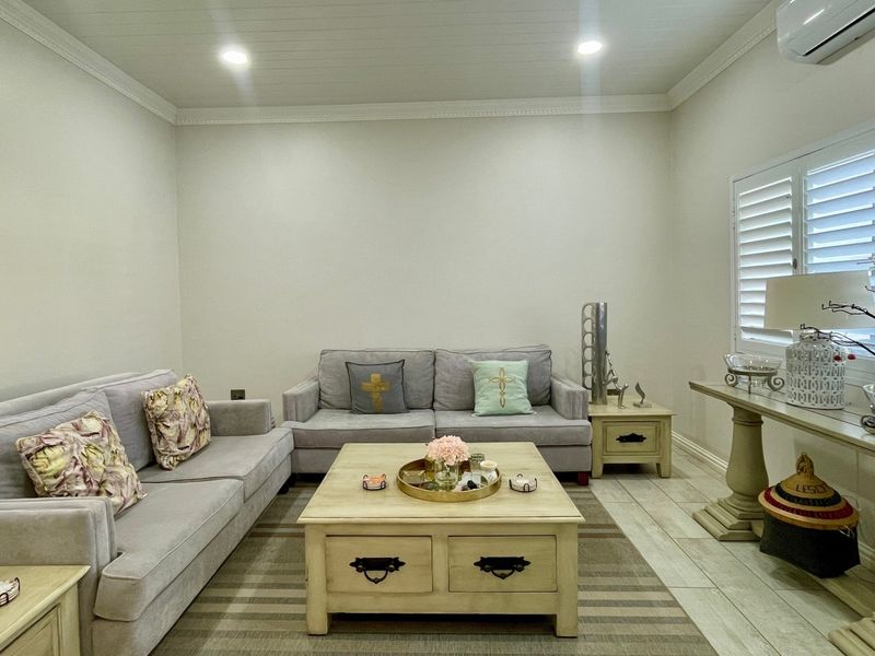 A well-maintained living room featuring tiled flooring, plantation shutters, crown molding, and a tongue and groove ceiling with recessed lighting.
