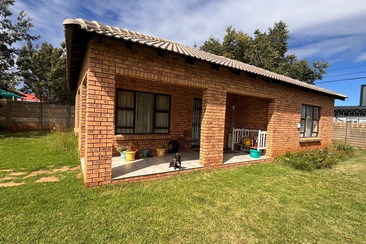 A well-maintained face brick house featuring a covered patio, tiled roof, and a spacious surrounding garden with secure boundary walling.