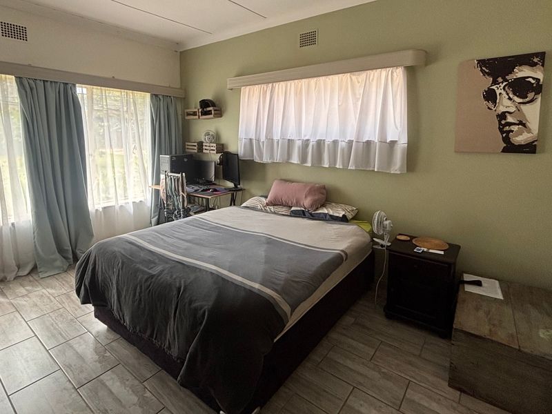 A bedroom featuring tiled flooring, large windows with curtain rails, and neutral wall finishes.