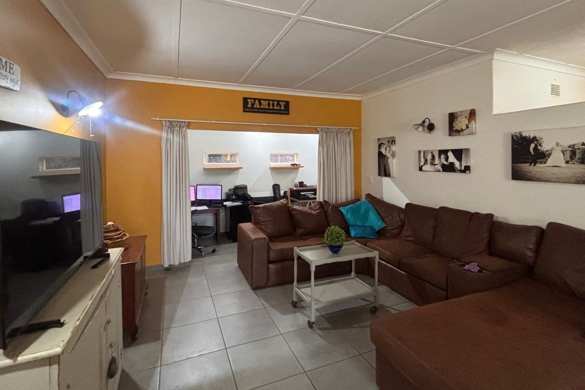 A spacious living room featuring tiled flooring and a coved ceiling, with an open transition to an adjacent office or study area.