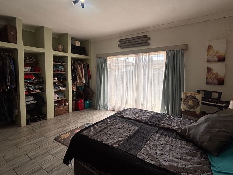 Spacious bedroom featuring built-in open shelving units, tiled flooring, and large windows with curtain treatments, offering ample storage and natural light.