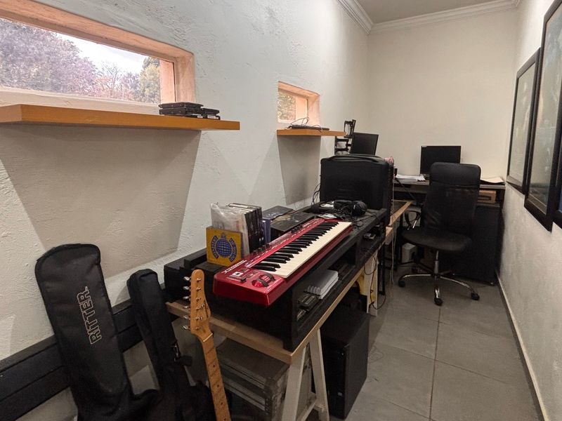 A compact home office or studio space featuring tiled flooring, crown molding, and high-set windows providing natural light.