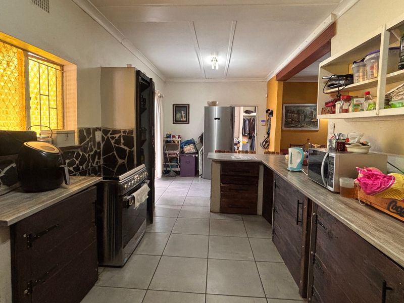 A functional kitchen featuring stone-clad splashbacks, laminate countertops, and ample built-in cabinetry with open shelving, finished with ceramic floor tiles.