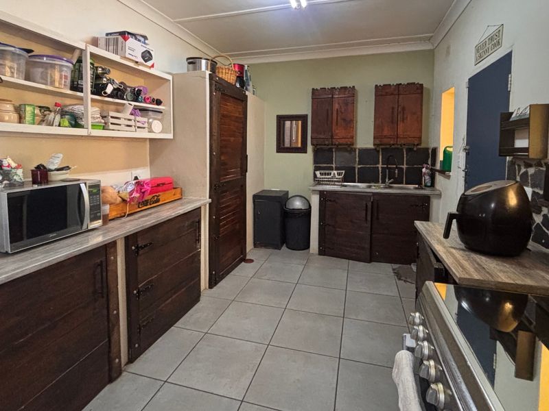 A functional kitchen featuring dark wood cabinetry, laminate countertops, tiled backsplash, and ceramic flooring, offering potential for a modern cosmetic update.