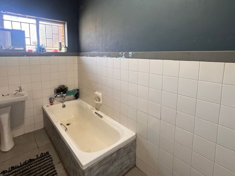 A functional bathroom featuring a pedestal basin and a built-in bathtub with tiled wall surrounds, requiring cosmetic updates to the wall finishes and fixtures.