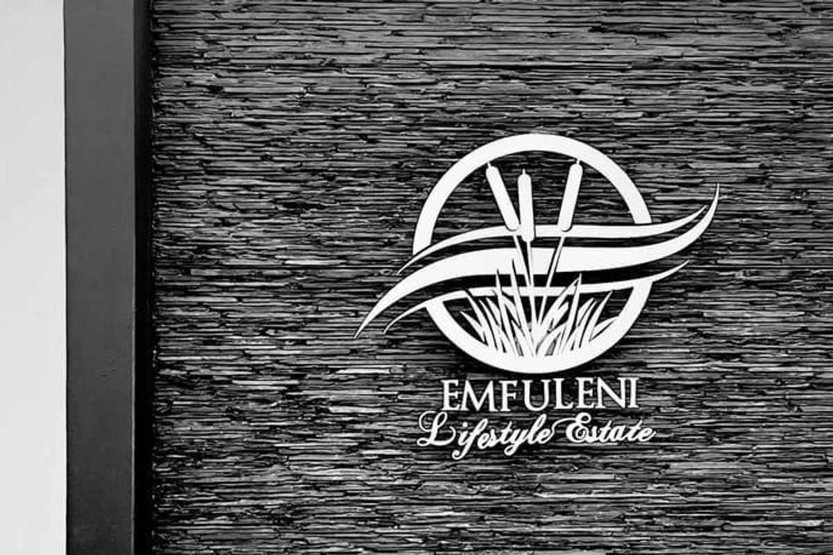 A close-up view of a textured stacked stone wall featuring the Emfuleni Lifestyle Estate logo.