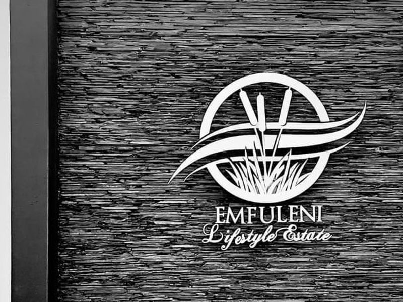 A close-up view of a textured stacked stone wall featuring the Emfuleni Lifestyle Estate logo.