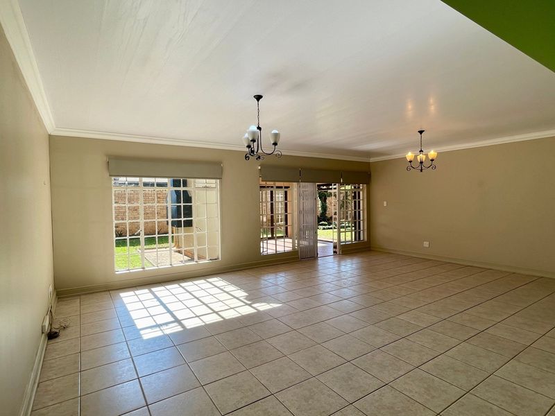 Spacious, light-filled living area featuring neutral ceramic tile flooring, classic ceiling chandeliers, and large lattice windows with direct access to the rear patio.