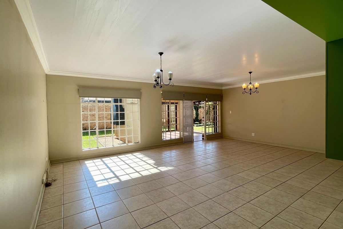 Spacious, light-filled living area featuring neutral ceramic tile flooring, classic ceiling chandeliers, and large lattice windows with direct access to the rear patio.