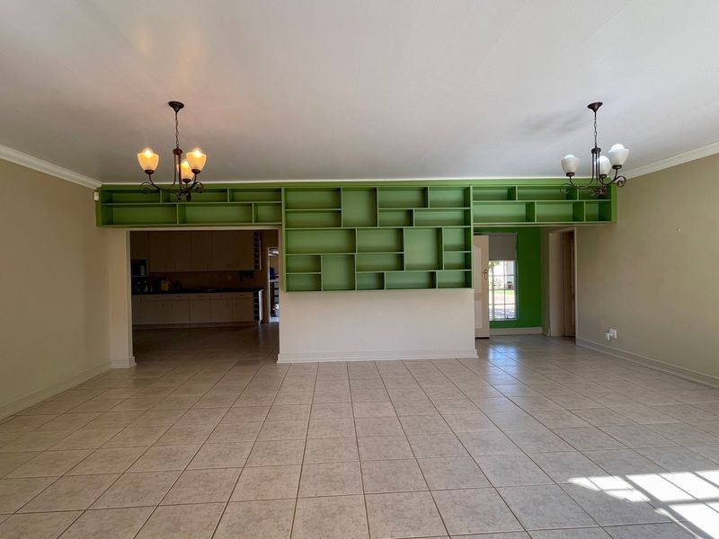 Spacious open-plan living area featuring neutral ceramic floor tiles, decorative cove cornicing, and a prominent built-in green shelving unit.
