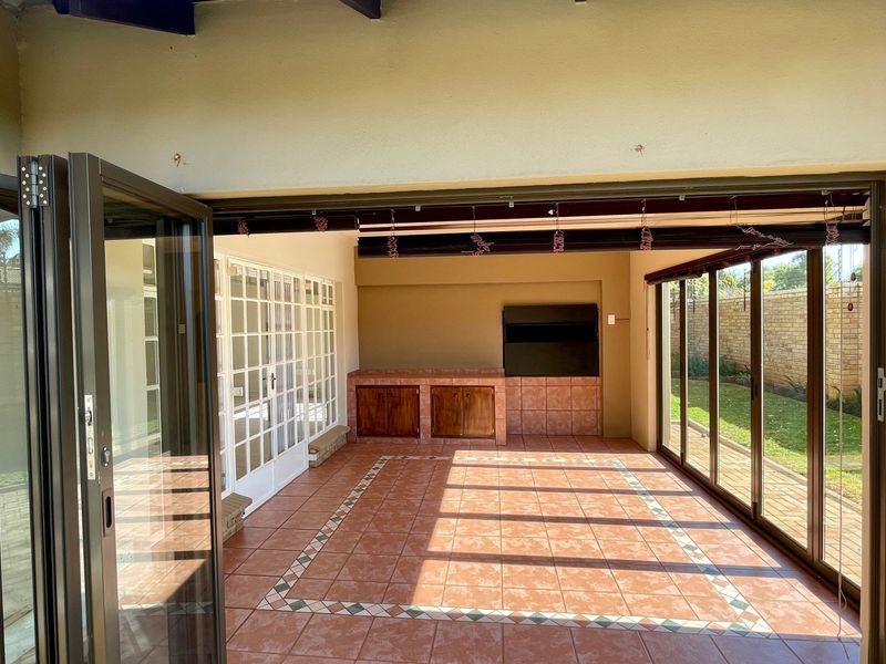 Spacious covered patio featuring tiled flooring, a built-in braai, and extensive glass folding and sliding doors providing seamless indoor-outdoor flow.
