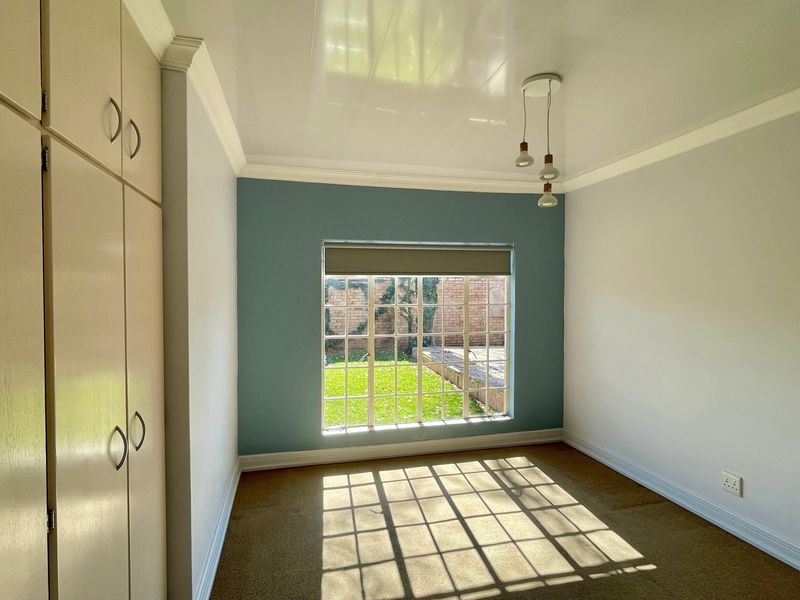 A bright, empty bedroom featuring built-in cupboards, a feature wall, and a large grid-pattern window overlooking the garden.