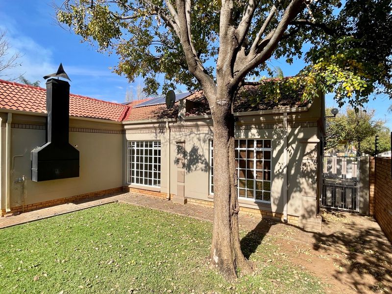 Rear exterior view of the townhouse featuring a private garden, paved patio area, built-in braai, and solar panels on the roof.