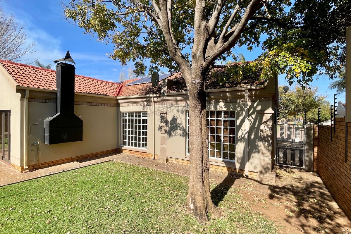 Rear exterior view of the townhouse featuring a private garden, paved patio area, built-in braai, and solar panels on the roof.