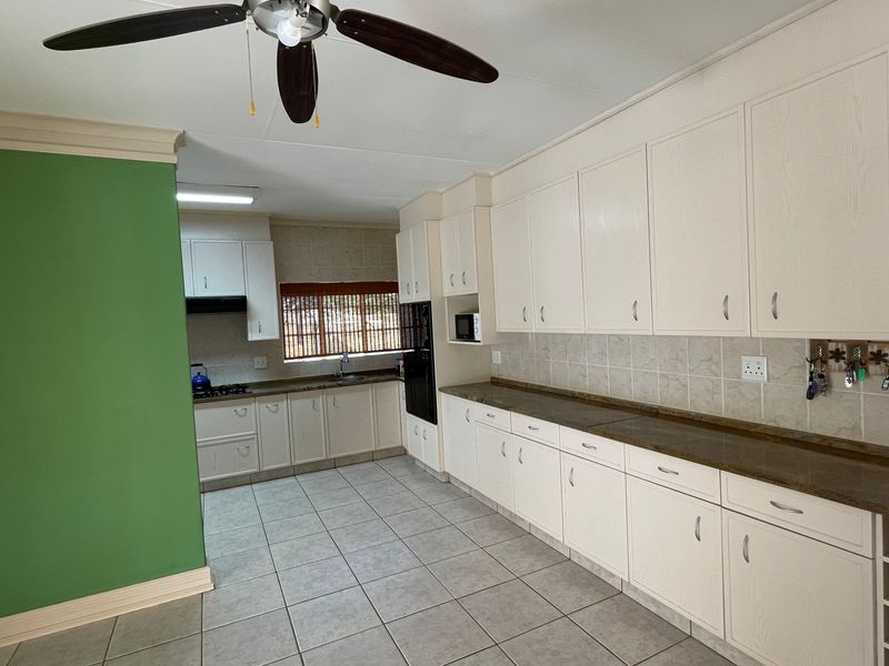 Spacious kitchen featuring extensive built-in cabinetry, laminate countertops, tiled flooring, and integrated appliances, offering a functional layout with ample storage space.