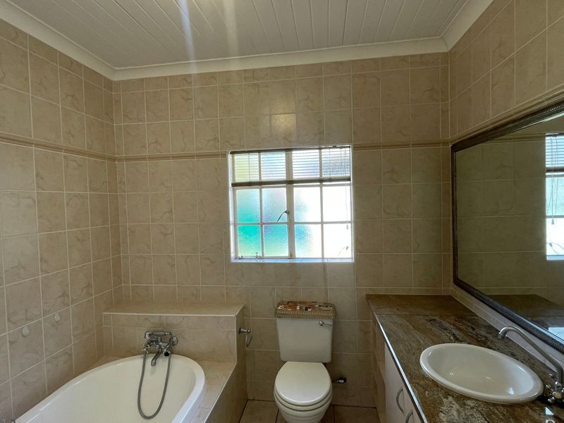 A functional bathroom featuring a built-in bathtub, a vanity with a stone countertop, and neutral wall tiling throughout.