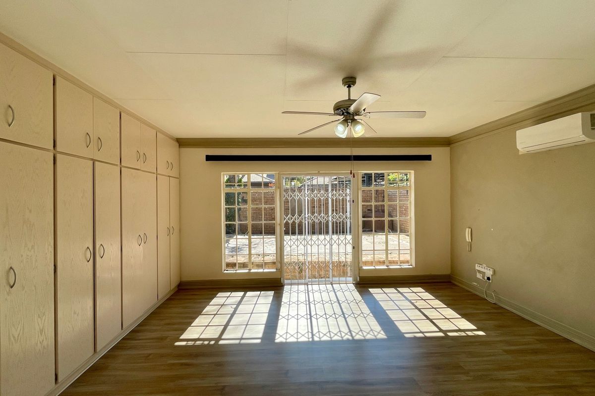 Spacious bedroom featuring extensive built-in cabinetry, laminate flooring, a ceiling fan, and a wall-mounted air conditioning unit with direct access to the rear exterior.