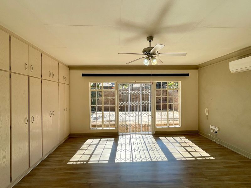 Spacious bedroom featuring extensive built-in cabinetry, laminate flooring, a ceiling fan, and a wall-mounted air conditioning unit with direct access to the rear exterior.