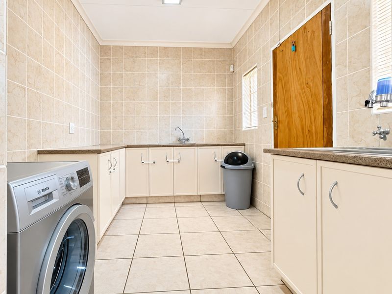 A functional laundry room featuring tiled walls and floors, ample built-in cabinetry, laminate countertops, and a stainless steel sink.