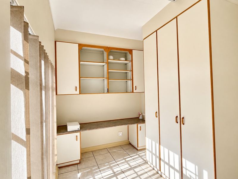 A functional home office space featuring built-in cabinetry, a desk area, and tiled flooring, offering ample storage and a clean, neutral aesthetic.