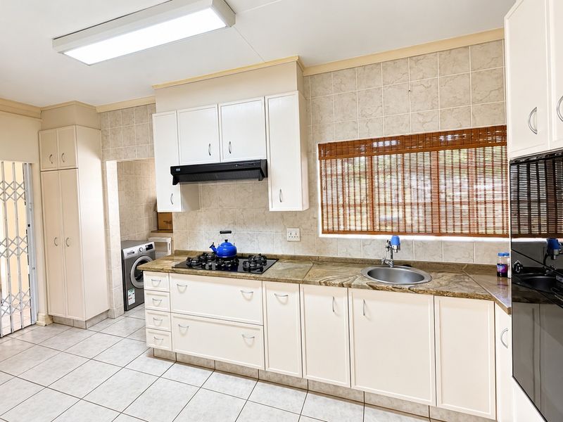 A functional kitchen featuring white cabinetry, stone countertops, a gas hob, built-in oven, and tiled flooring, with an adjacent laundry area.