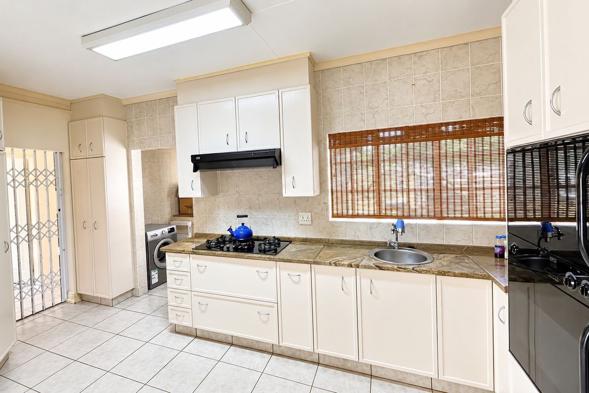 A functional kitchen featuring white cabinetry, stone countertops, a gas hob, built-in oven, and tiled flooring, with an adjacent laundry area.