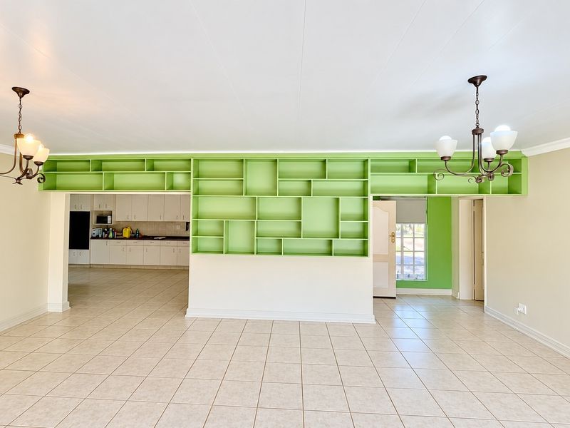 Spacious open-plan living area featuring tiled floors, decorative pendant lighting, and a large built-in green shelving unit, with an adjoining kitchen space.