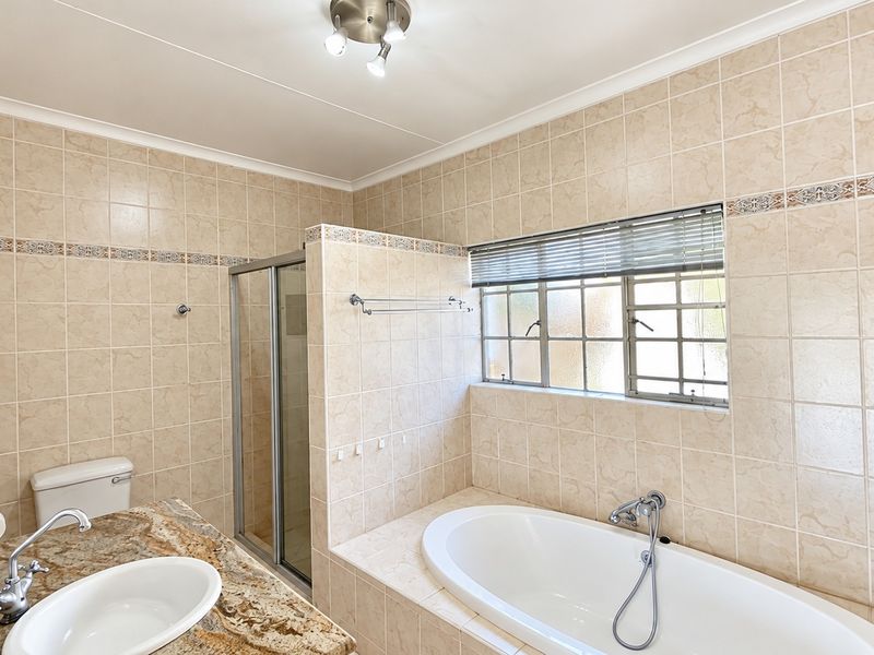 A functional bathroom featuring a built-in bathtub, separate shower enclosure, and a vanity countertop with neutral ceramic wall tiling throughout.